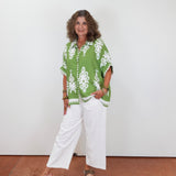 Woman wearing a green patterned shirt and white pants against a plain background