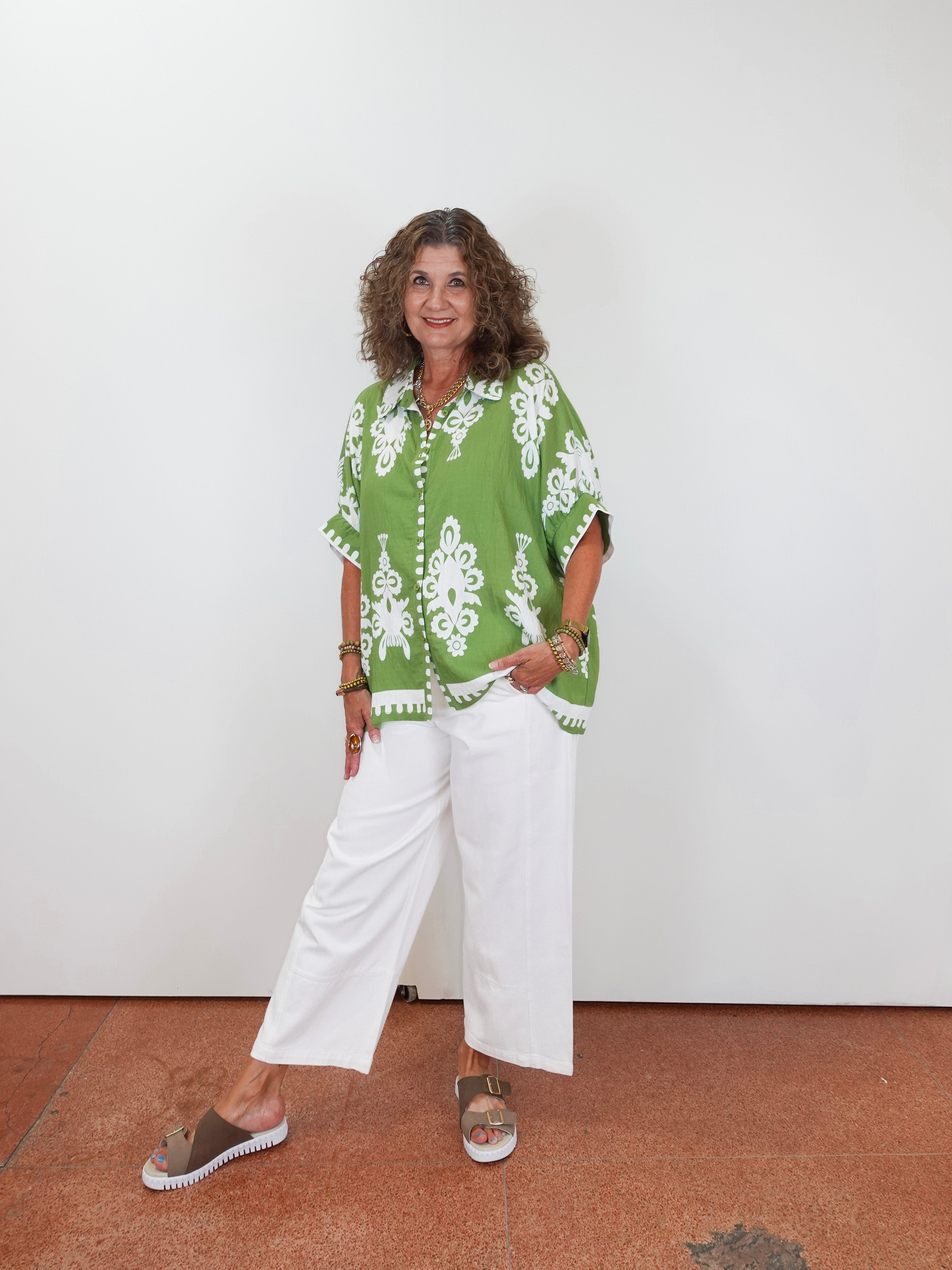 Woman wearing a green patterned shirt and white pants against a plain background