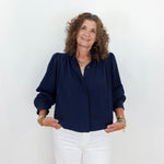 Woman wearing a navy blue blouse and white pants against a white background