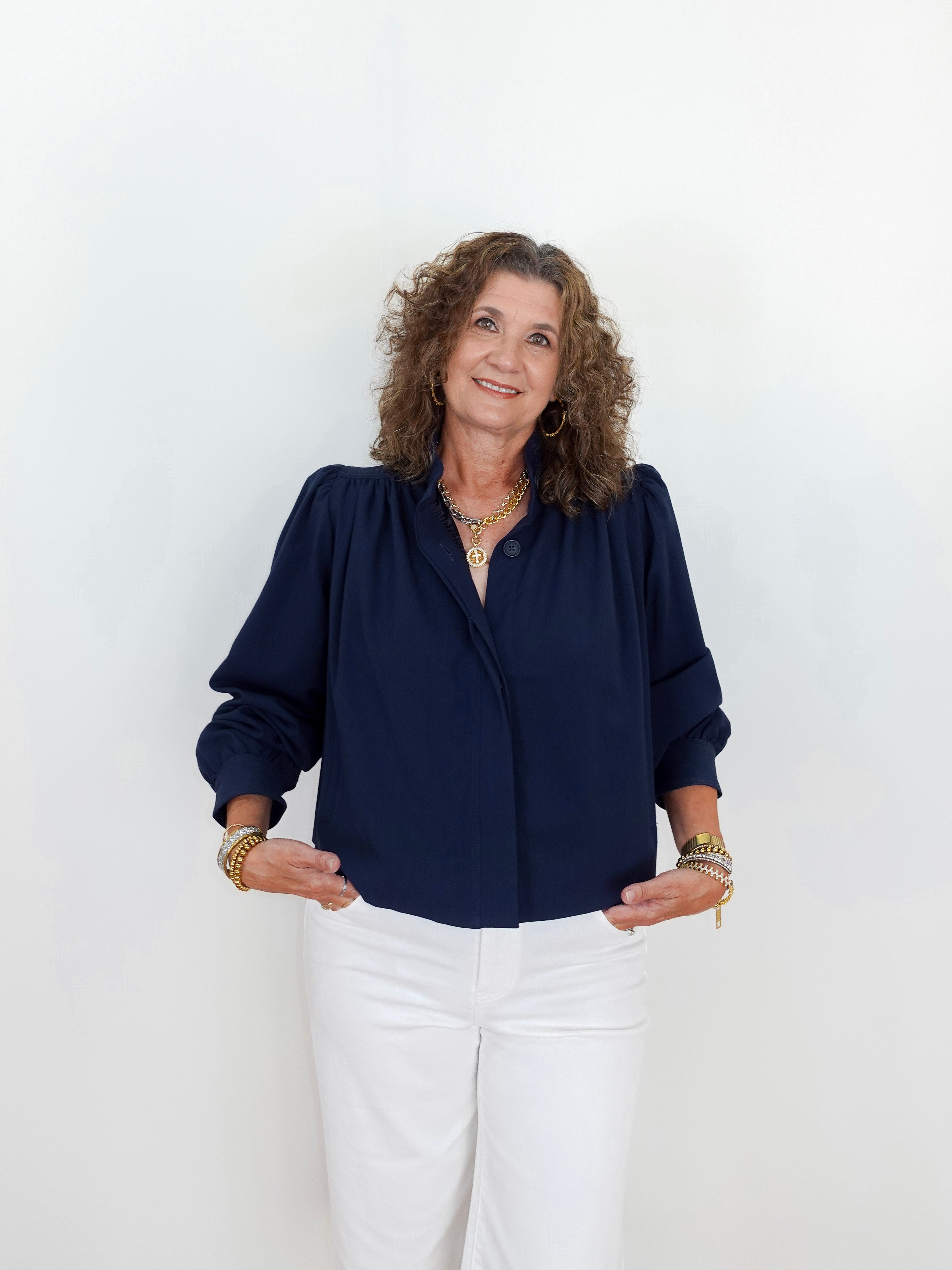 Woman wearing a navy blue blouse and white pants against a white background