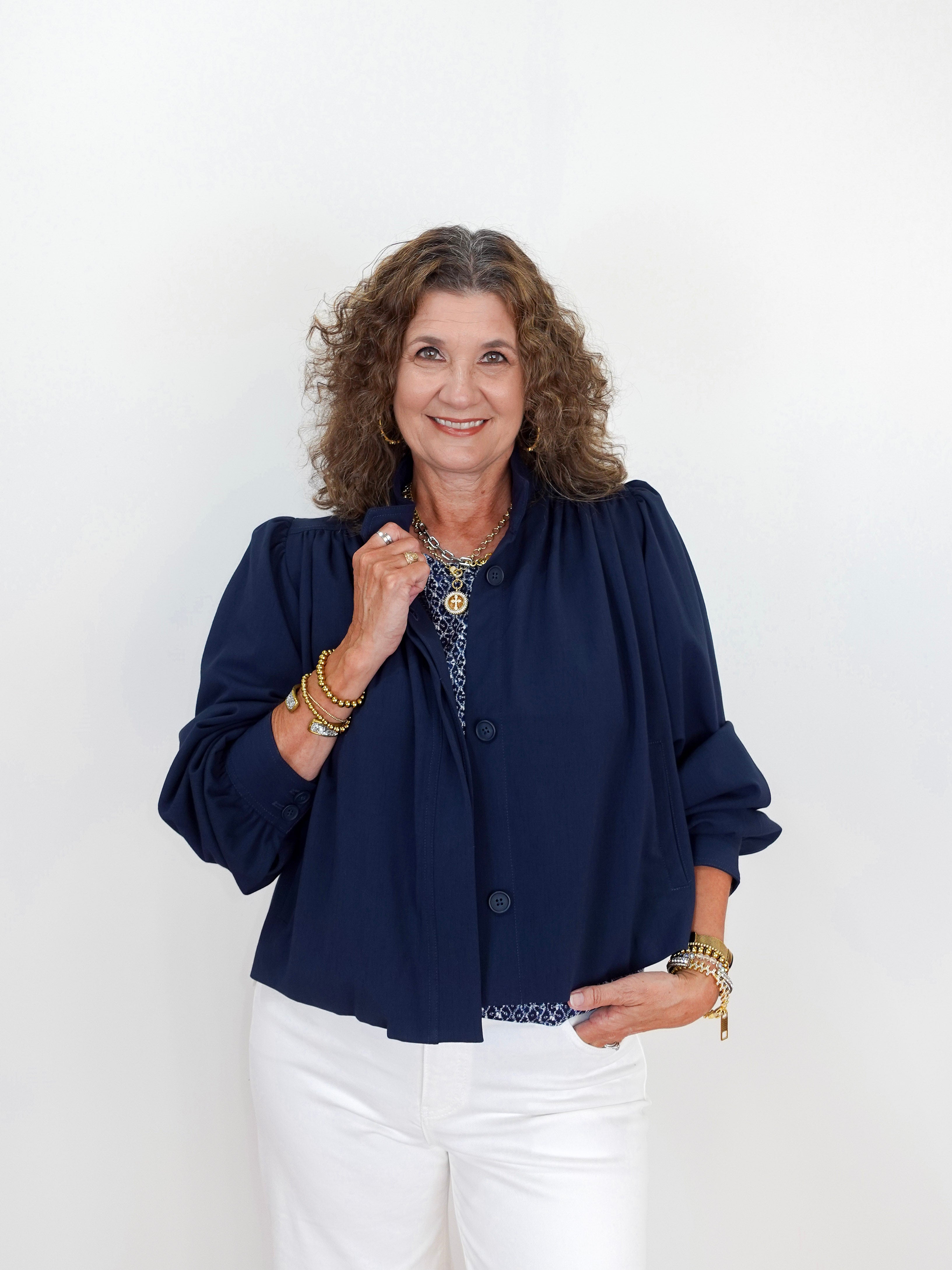 Woman wearing a navy blue jacket and white pants against a white background