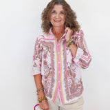 Woman wearing a pink and white patterned blouse with beige shorts, holding a pink handbag on a white background.