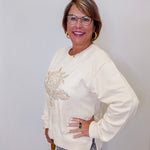 Woman wearing a cream-colored sweater with embroidery, standing against a plain background
