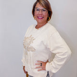 Woman wearing a cream-colored sweater with embroidery, standing against a plain background