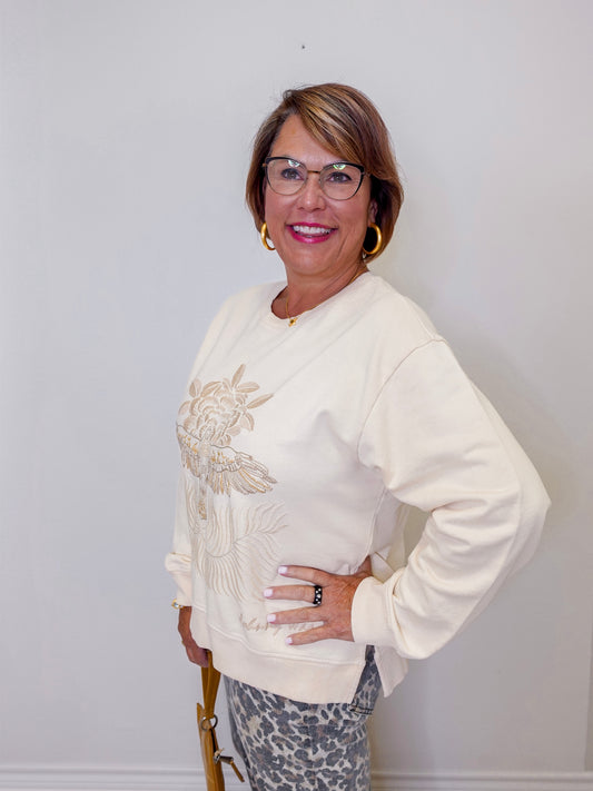 Woman wearing a cream-colored sweater with embroidery, standing against a plain background
