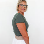 Woman wearing a green top and white pants against a plain background