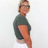 Woman wearing a green top and white pants against a plain background