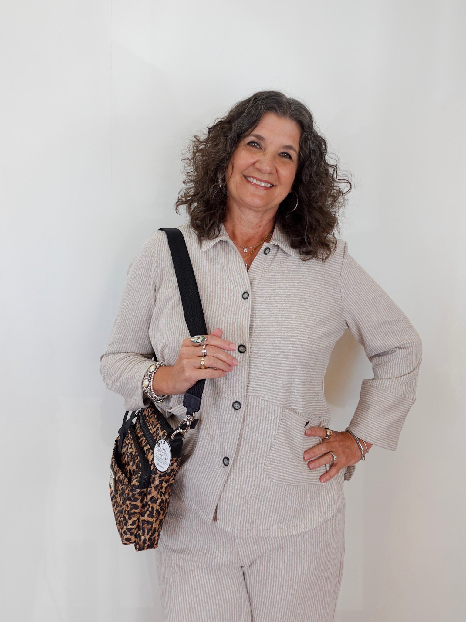 Woman in a light gray outfit with a leopard print bag against a white background