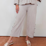 Person wearing a beige outfit with wide-leg pants and sandals on a plain background