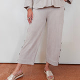 Person wearing a beige outfit with wide-leg pants and sandals on a plain background