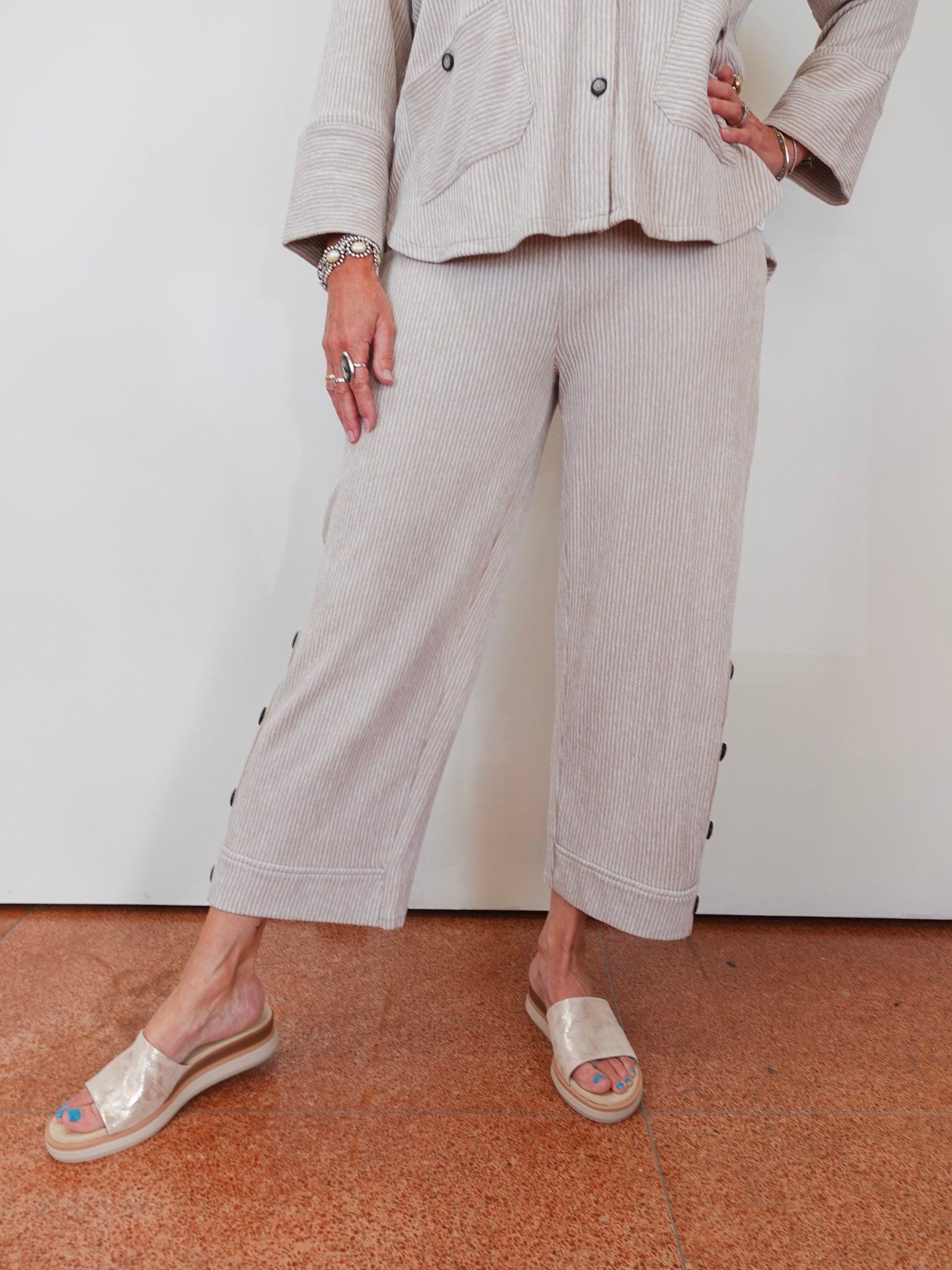 Person wearing a beige outfit with wide-leg pants and sandals on a plain background