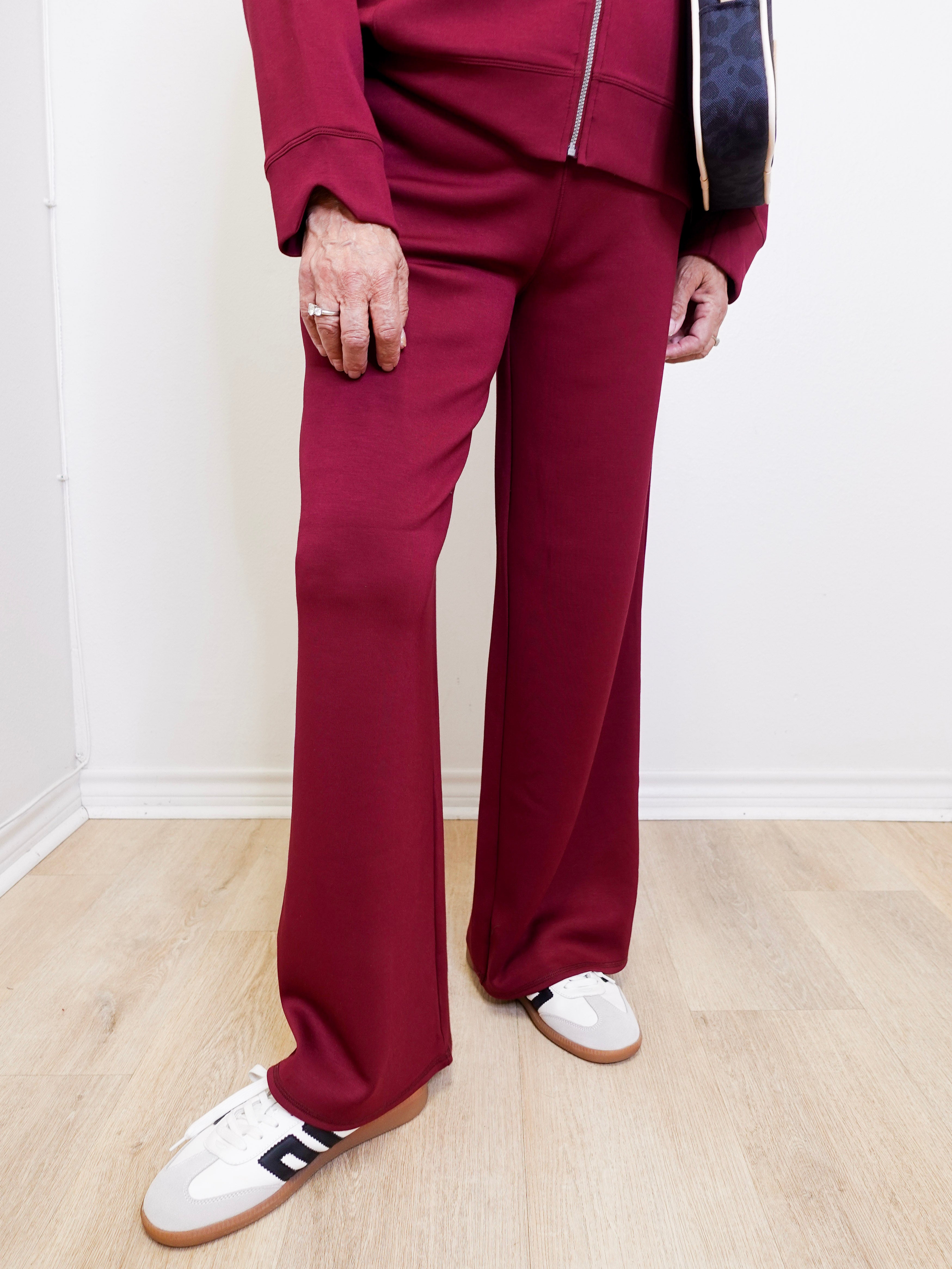 Person wearing a maroon tracksuit with white shoes on a light wooden floor.