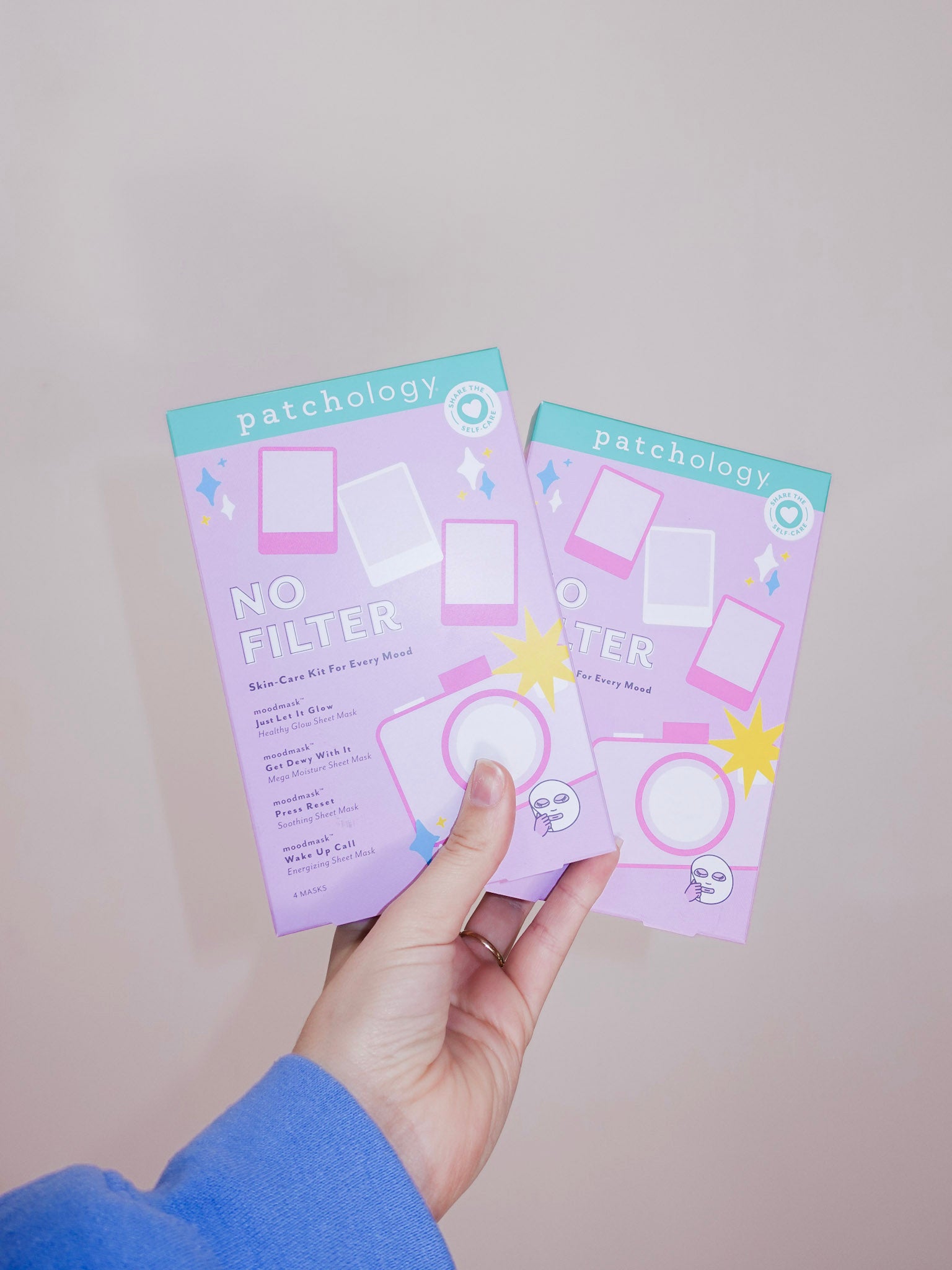 Two packages of 'No Filter' face masks held by a hand against a plain background