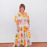 Woman wearing a colorful, patterned dress against a white wall.