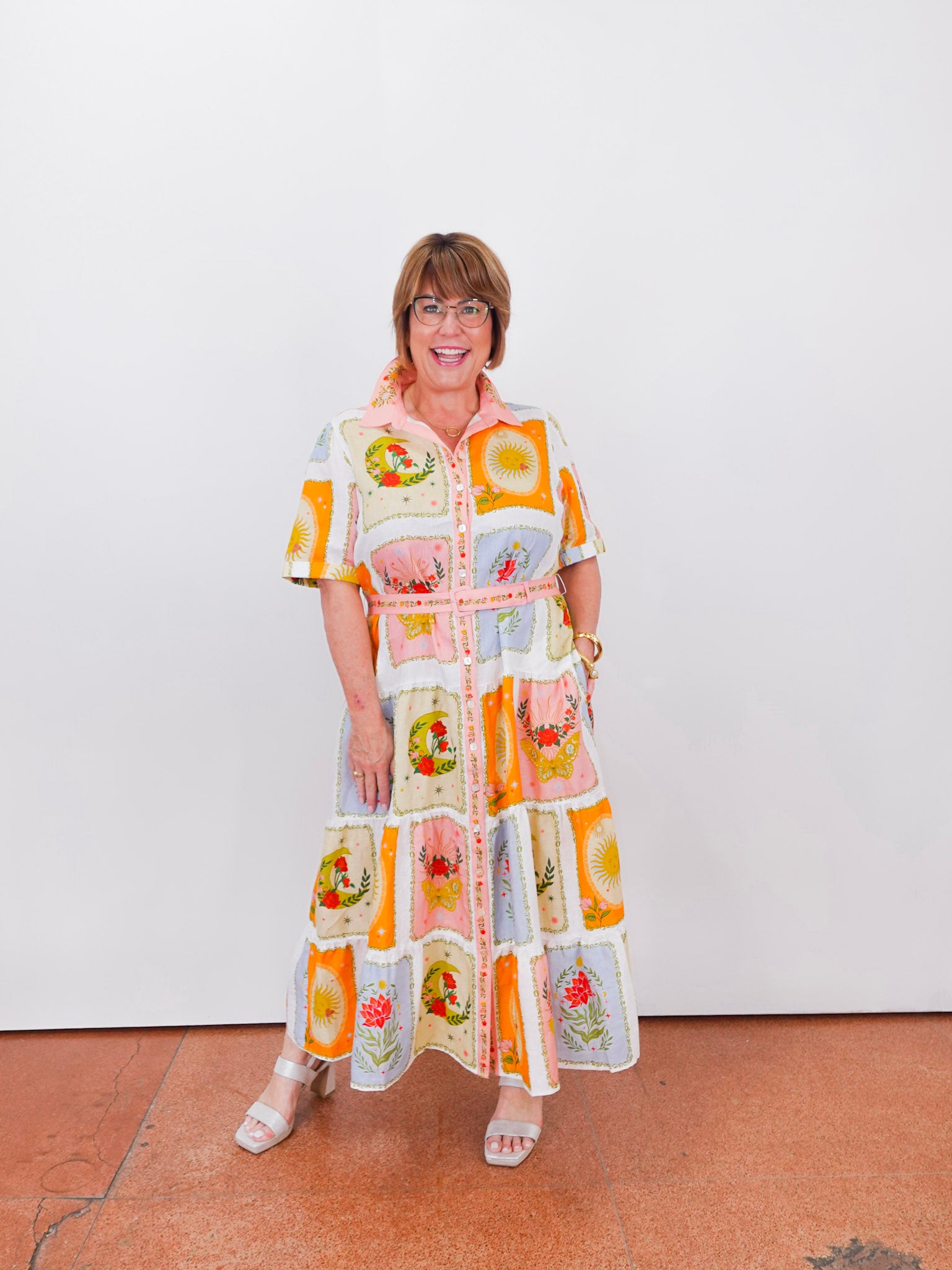 Woman wearing a colorful, patterned dress against a white wall.
