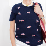 Woman wearing a navy blue t-shirt with small flag patterns, holding a red bag against a white background.