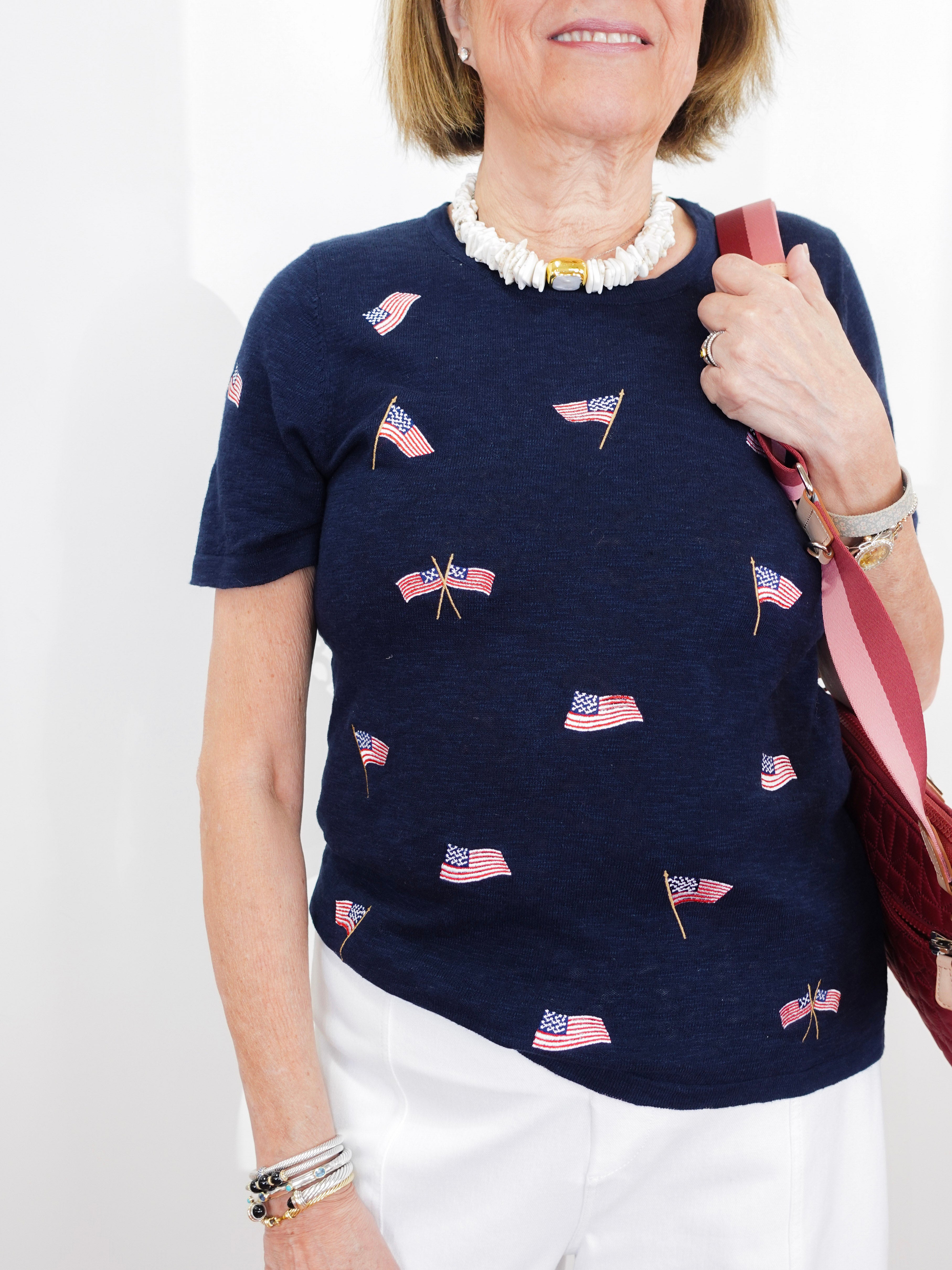Woman wearing a navy blue t-shirt with small flag patterns, holding a red bag against a white background.
