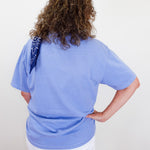 Person wearing a light blue t-shirt with a sequin detail on a plain background