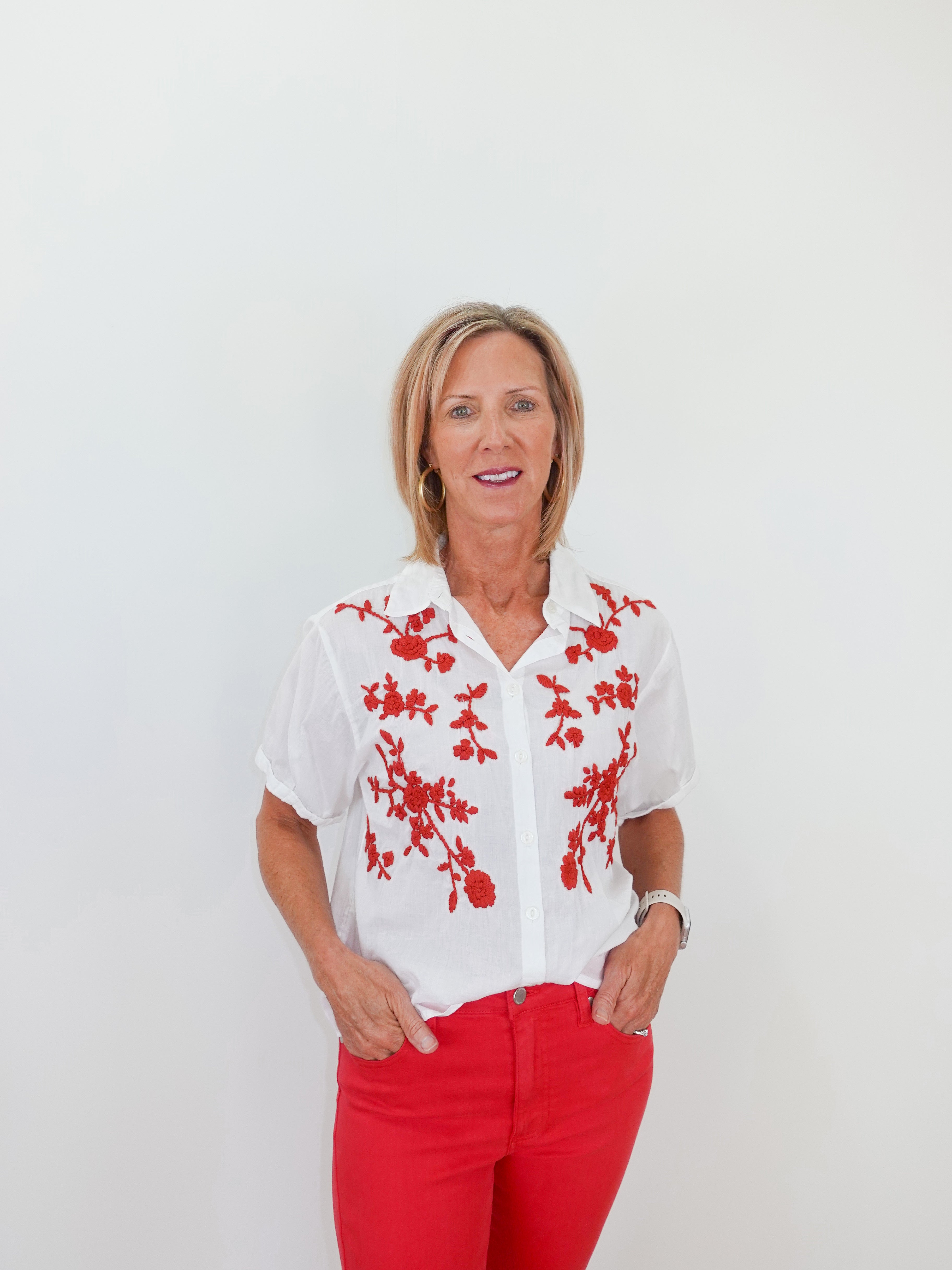 Woman wearing a white blouse with red floral patterns and red pants against a white background