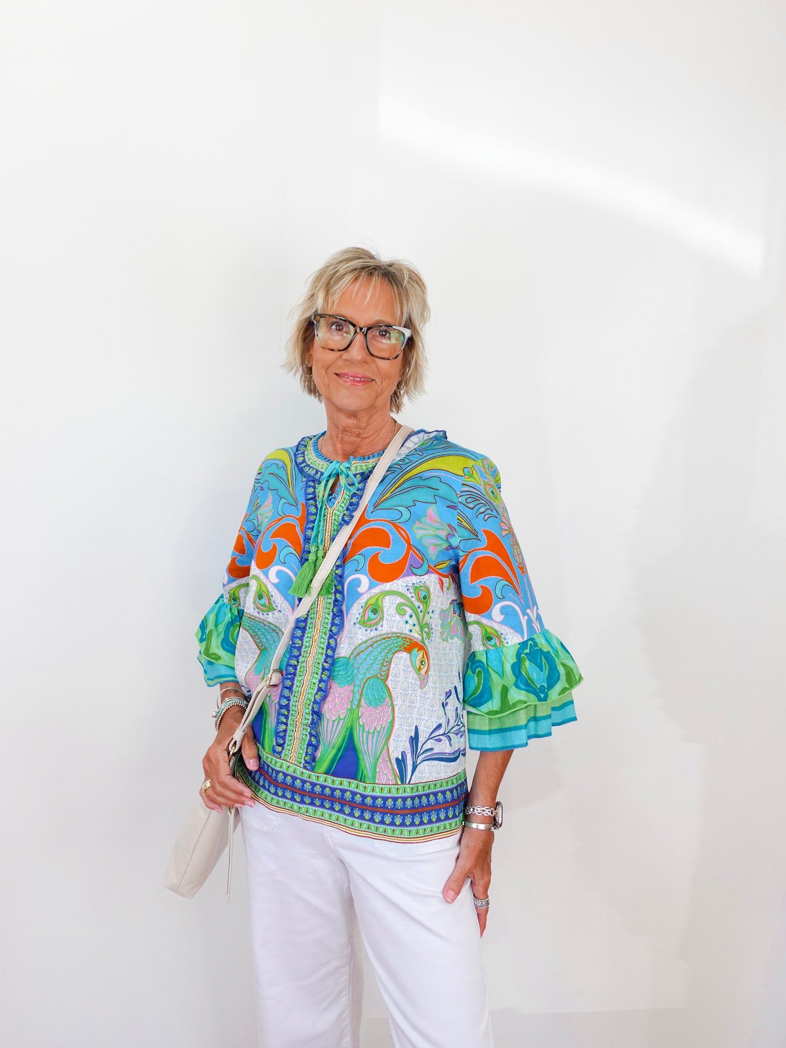 Woman wearing a colorful patterned top with white pants against a plain background
