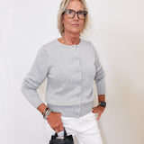 Woman wearing a gray sweater and white pants holding a black handbag against a white background