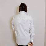 Person wearing a white jacket against a plain wall