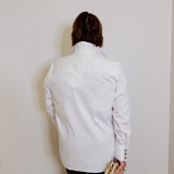 Person wearing a white jacket against a plain wall
