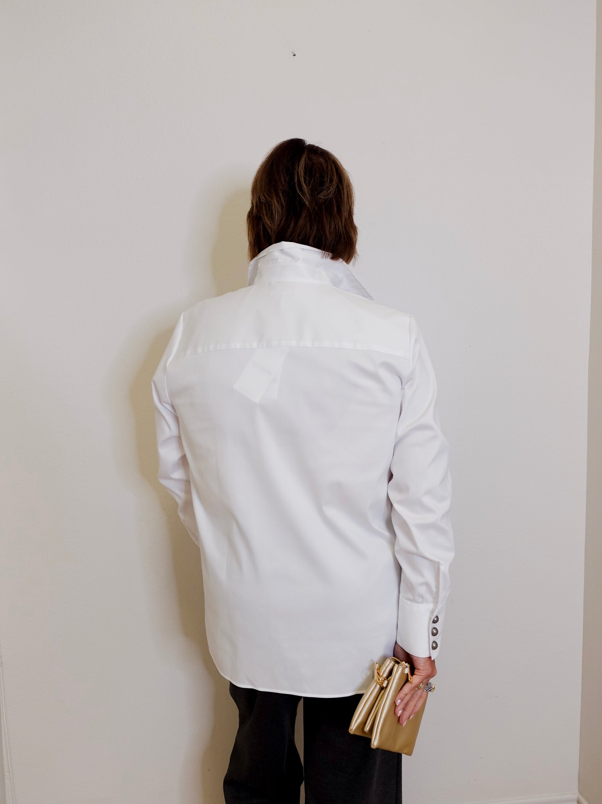 Person wearing a white jacket against a plain wall
