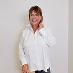 Woman wearing a white blouse and glasses, standing against a plain background