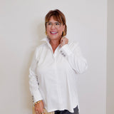 Woman wearing a white blouse and glasses, standing against a plain background
