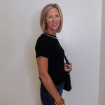Woman wearing a black top and blue jeans against a white wall