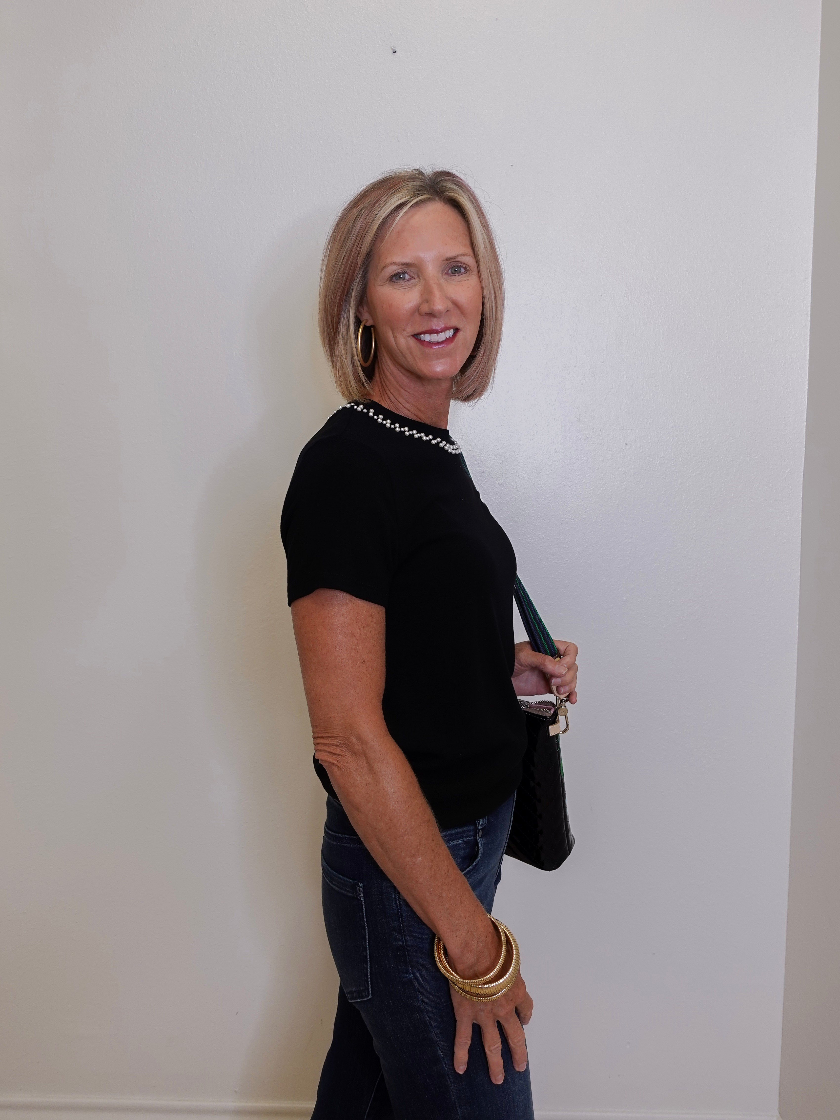 Woman wearing a black top and blue jeans against a white wall