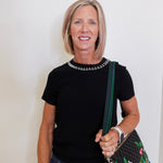 Woman wearing a black top with a studded collar, holding a colorful handbag against a plain background
