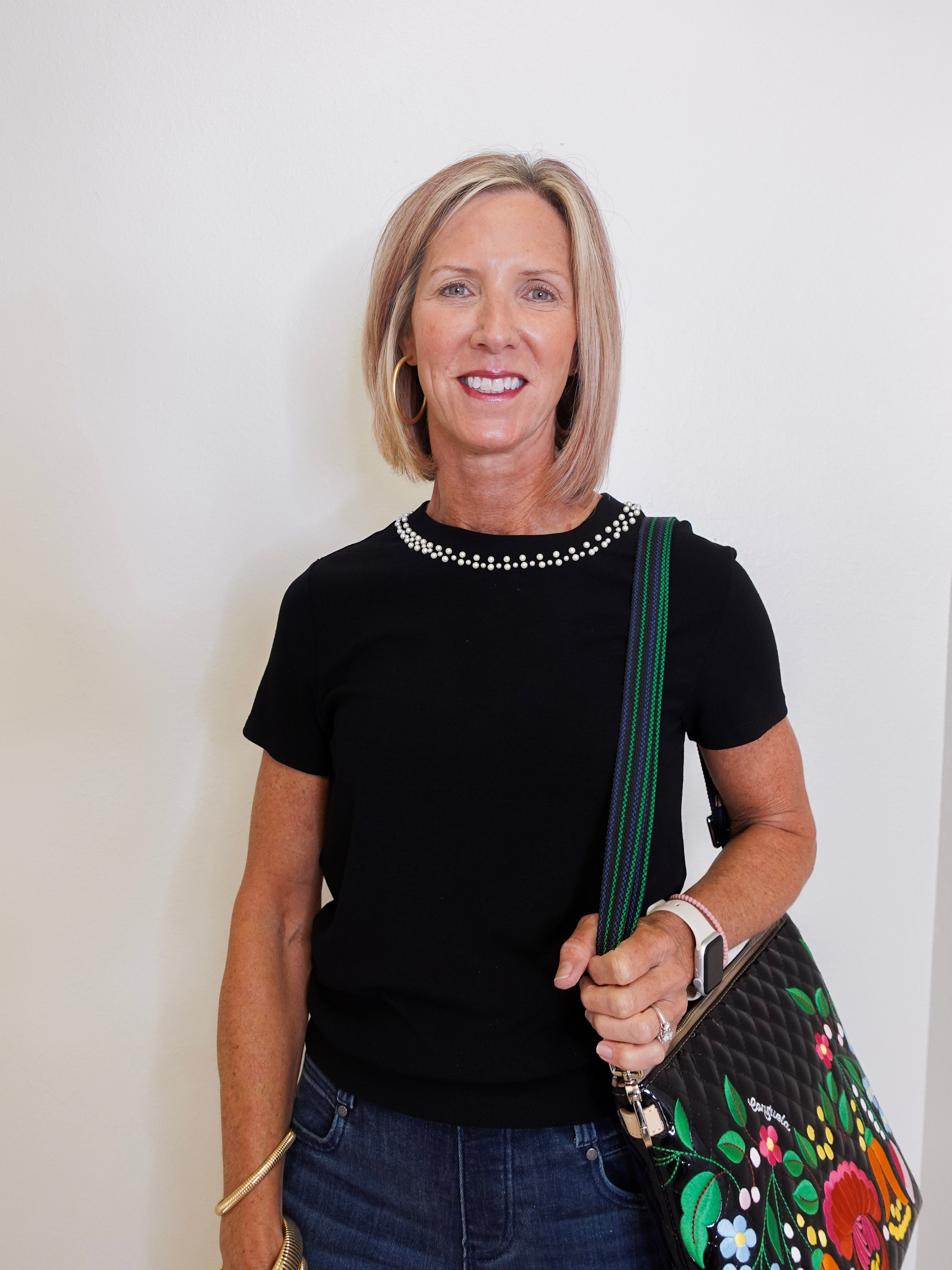 Woman wearing a black top with a studded collar, holding a colorful handbag against a plain background