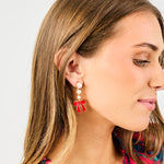 woman wearing pearl drop earrings with a red bow at the end against a white background. 