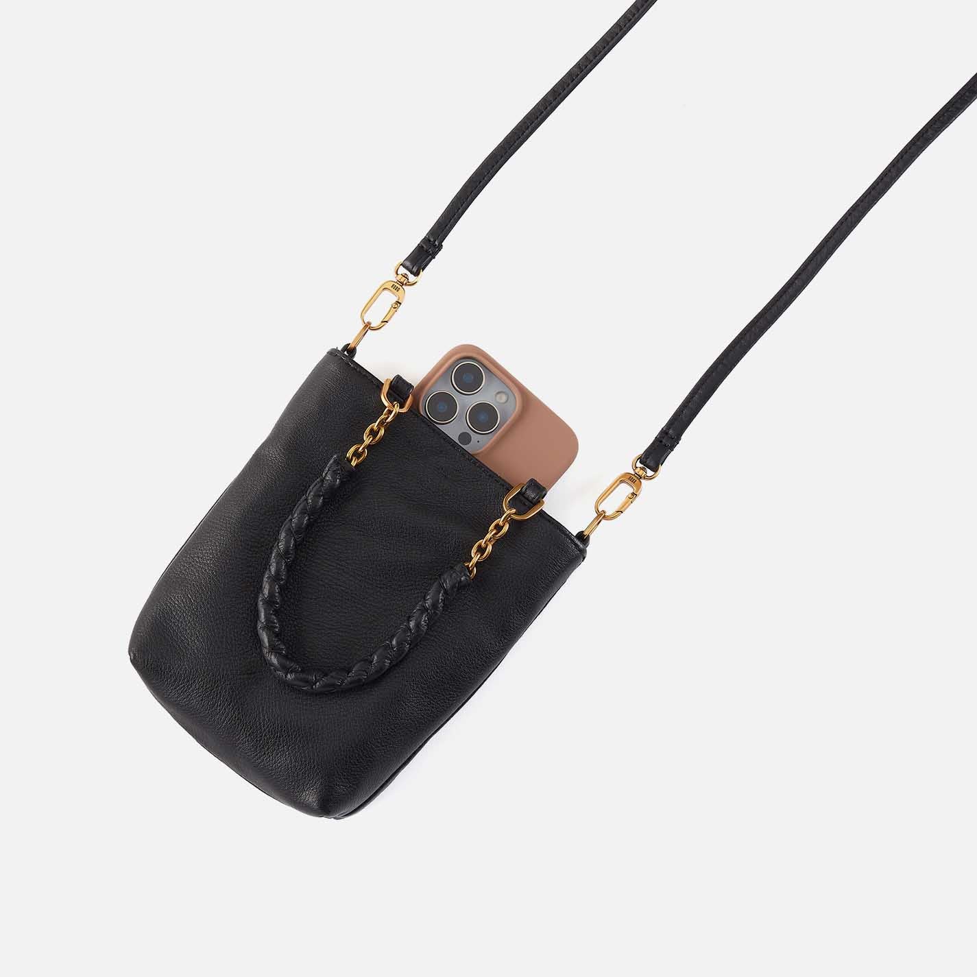 Black handbag with gold chain strap holding a phone on a light gray background