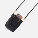 Black handbag with gold chain strap holding a phone on a light gray background