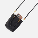 Black handbag with gold chain strap holding a phone on a light gray background