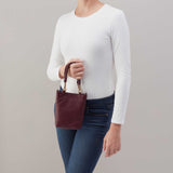 Person holding a maroon handbag against a neutral background