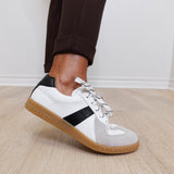 White sneakers with a black accent worn by a person on a wooden floor.