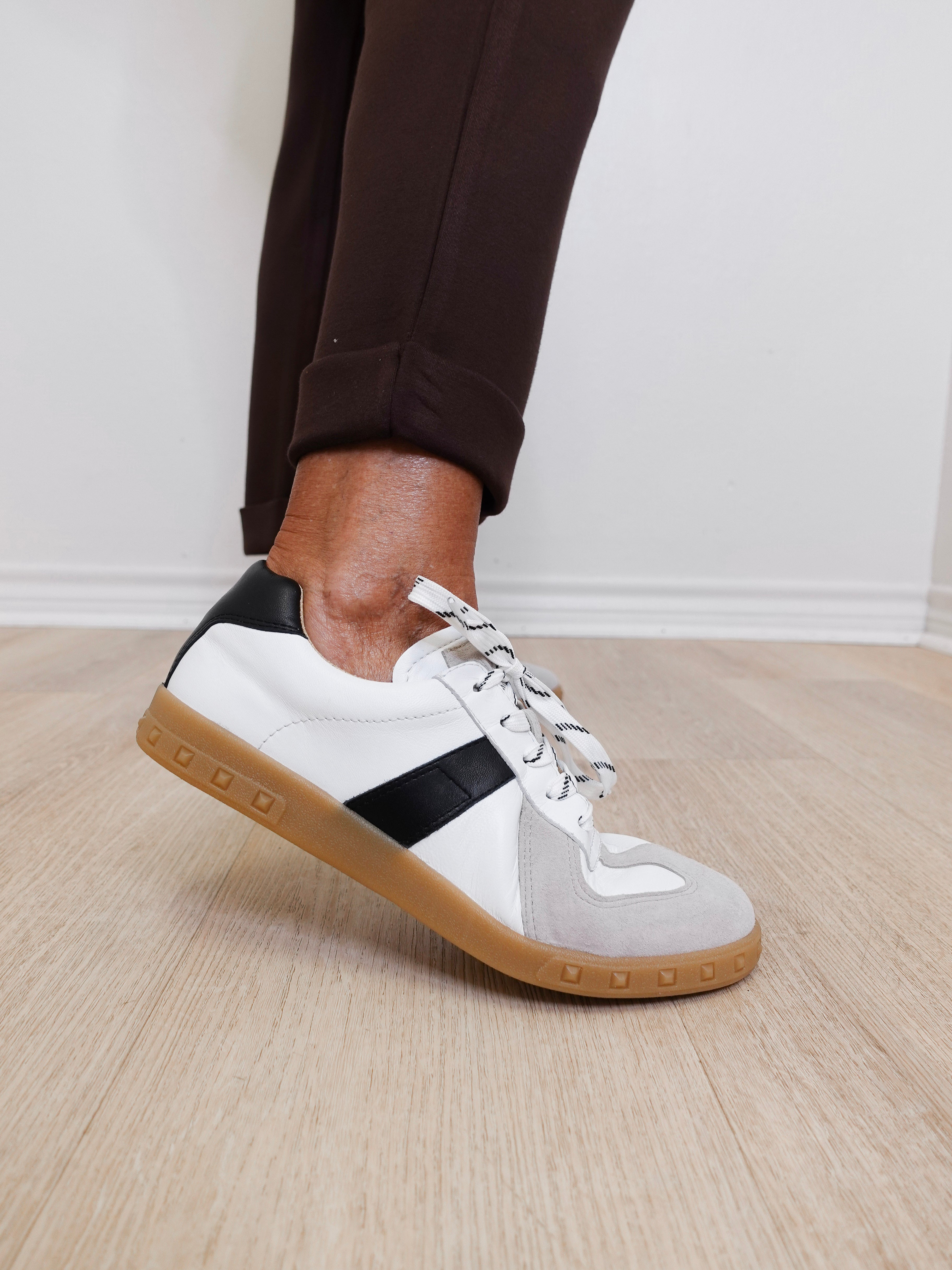 White sneakers with a black accent worn by a person on a wooden floor.