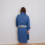 Person wearing a blue dress standing against a white wall.