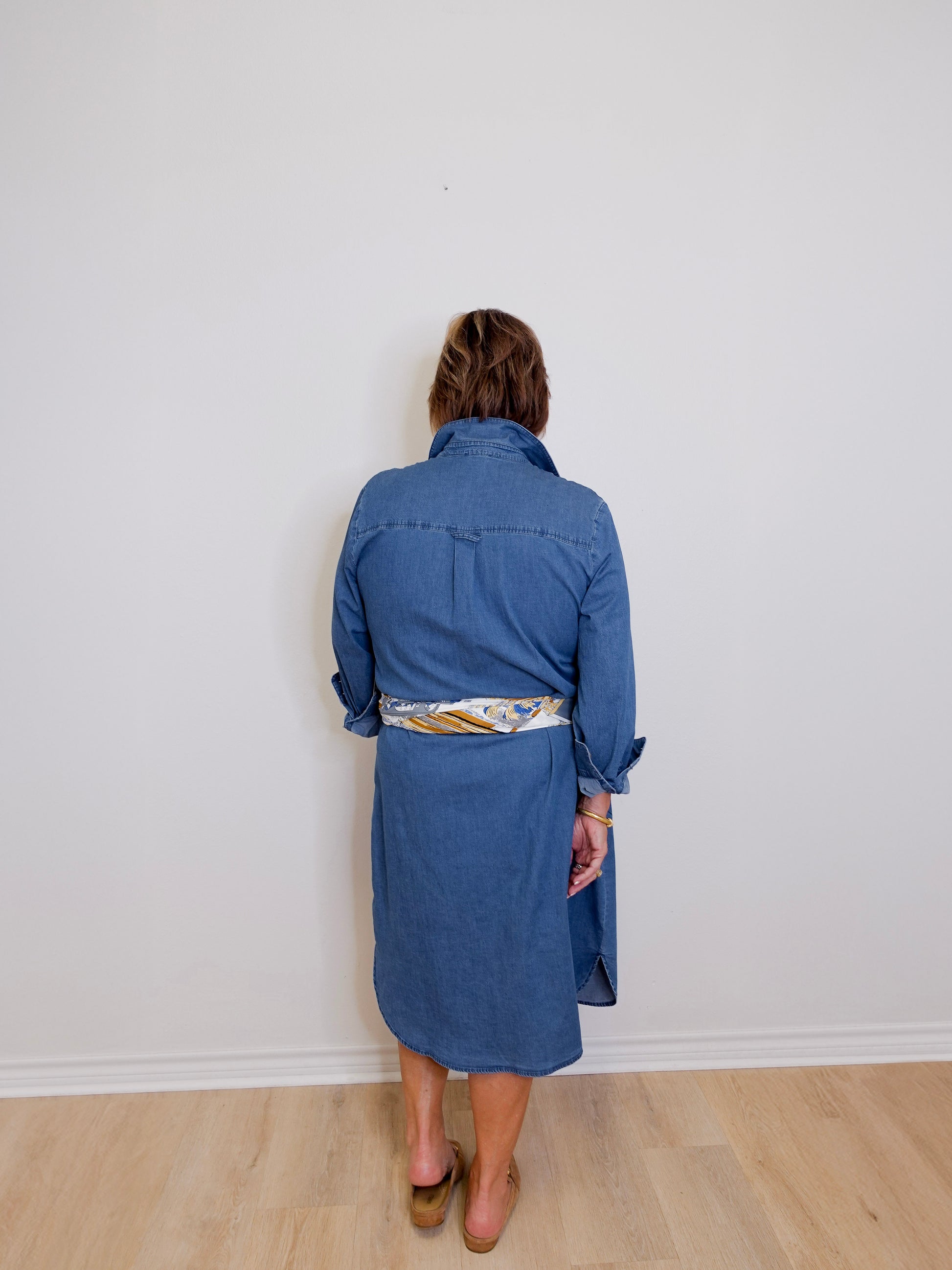 Person wearing a blue dress standing against a white wall.