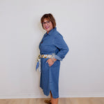 Person wearing a blue dress standing against a white wall.