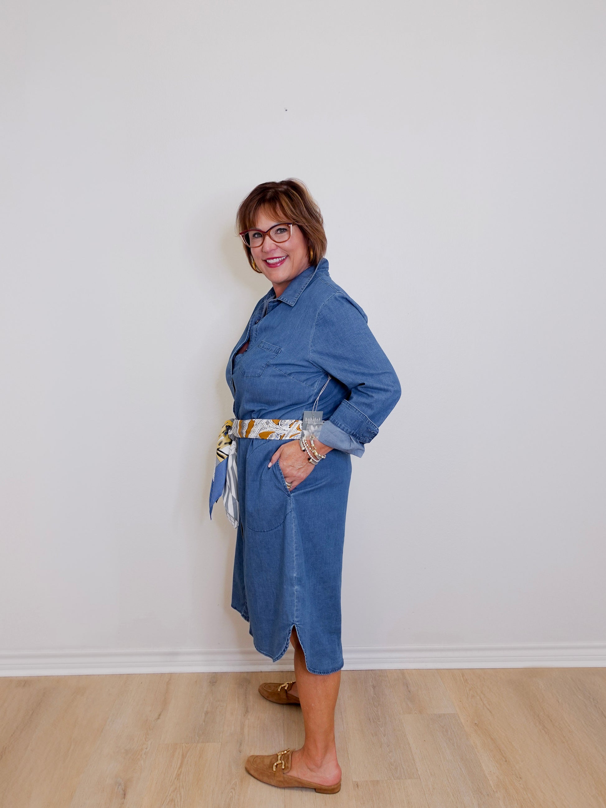 Person wearing a blue dress standing against a white wall.