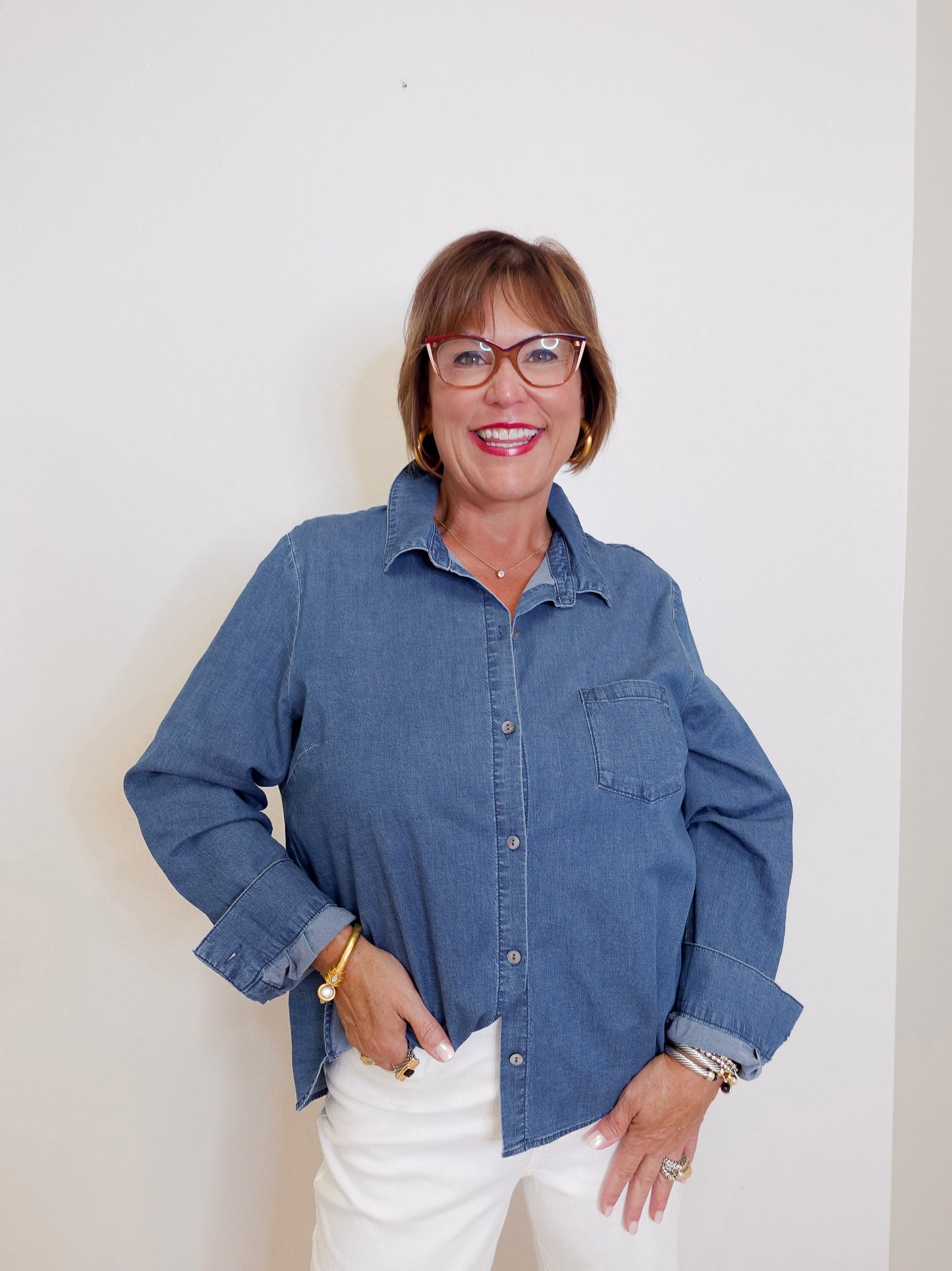 Woman wearing a blue denim shirt and white pants against a plain background