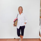 Woman in a white shirt and navy pants holding a folder against a white wall.