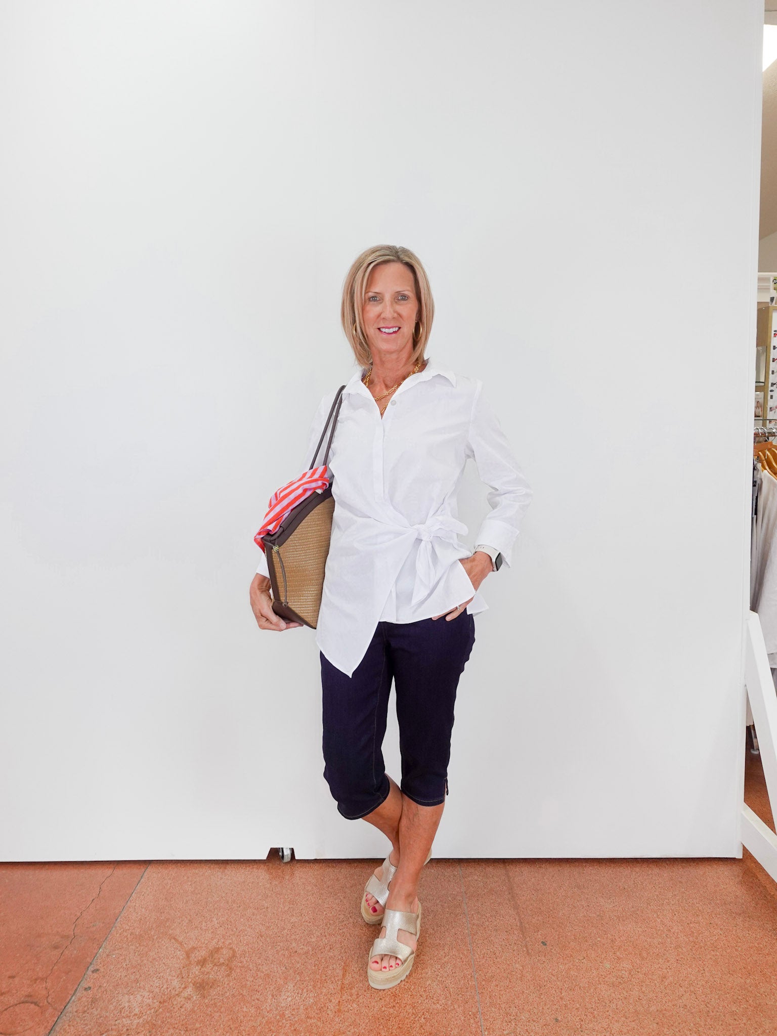 Woman in a white shirt and navy pants holding a folder against a white wall.