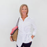 Woman wearing a white shirt and dark pants, holding a bag against a plain background