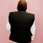 Person wearing a black vest over a white shirt on a pink background